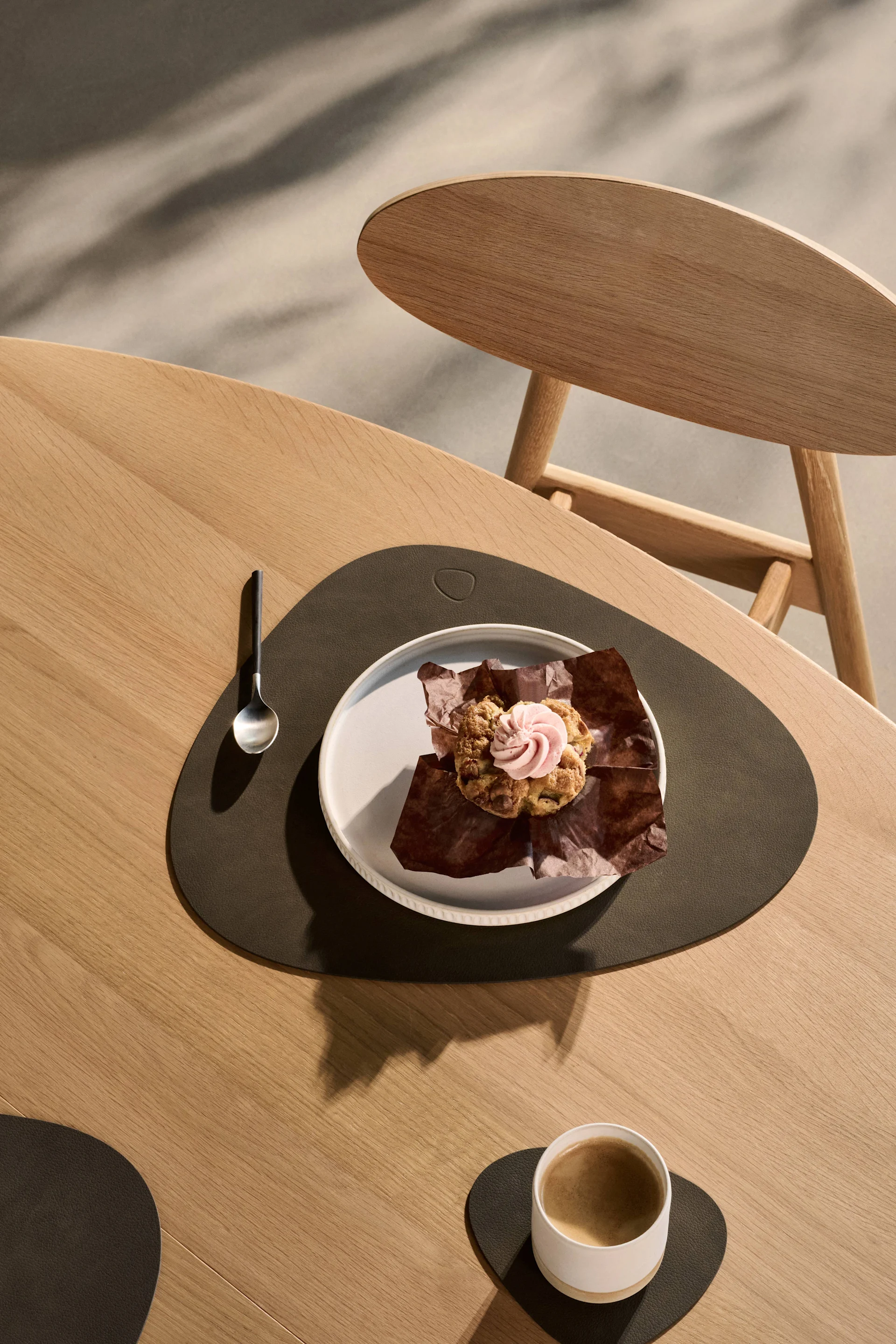 Muffin au glaçage rose et café sur une table en bois avec des sets de table et sous-verres foncés.