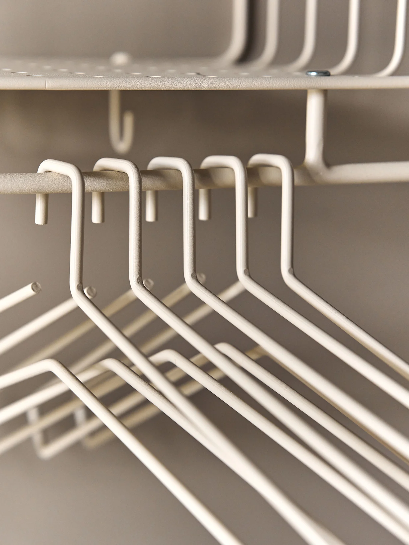 Un gros plan de plusieurs cintres métalliques vides de couleur crème suspendus à un porte-manteau en fil de fer.
