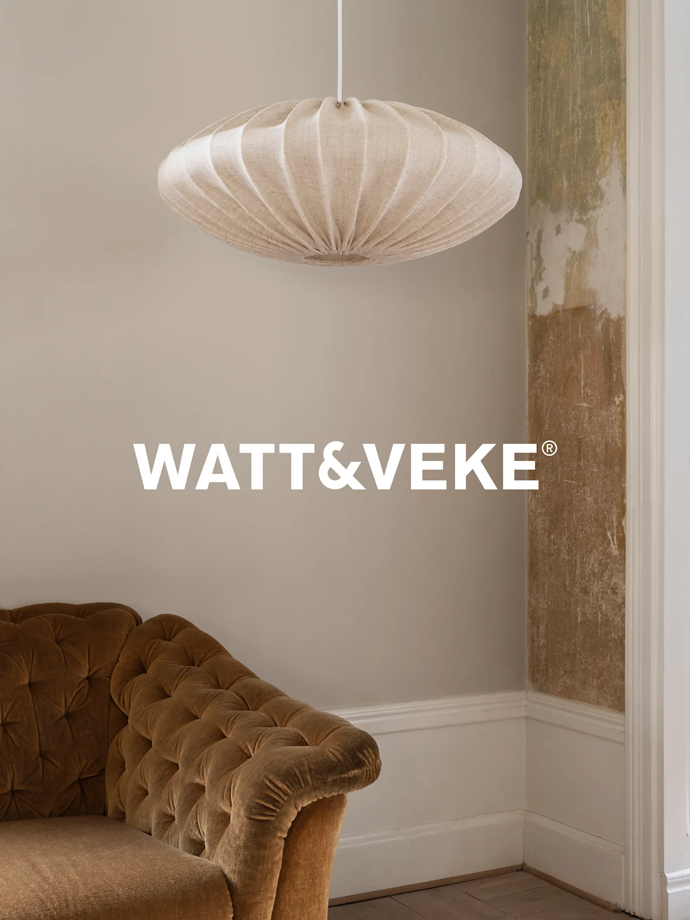 Une suspension en tissu plissé beige est suspendue au-dessus d'un canapé en velours marron dans une pièce au mur vieilli.