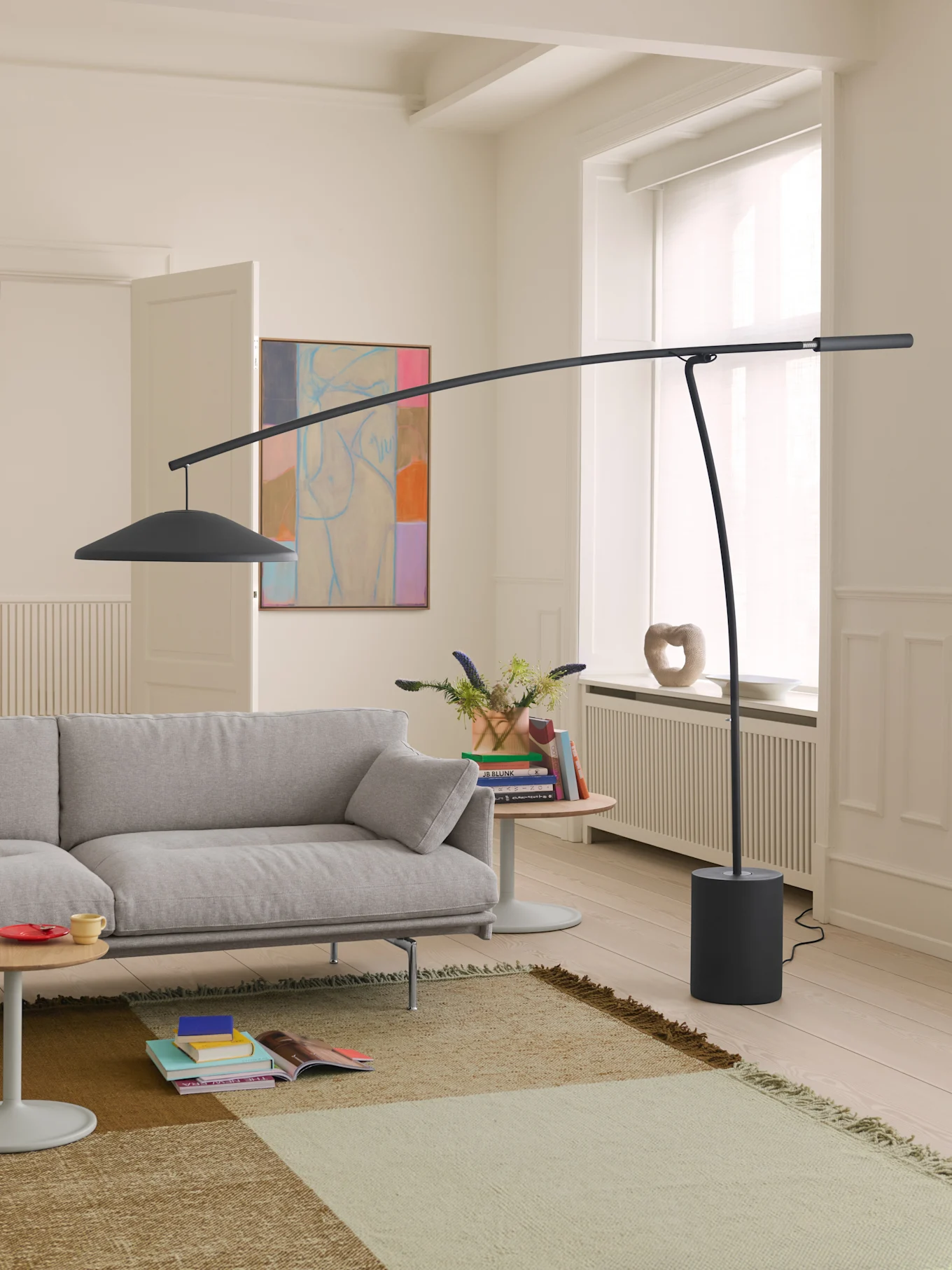 Salon moderne avec canapé gris clair, lampadaire arqué gris foncé et tapis à motifs sur un parquet clair.