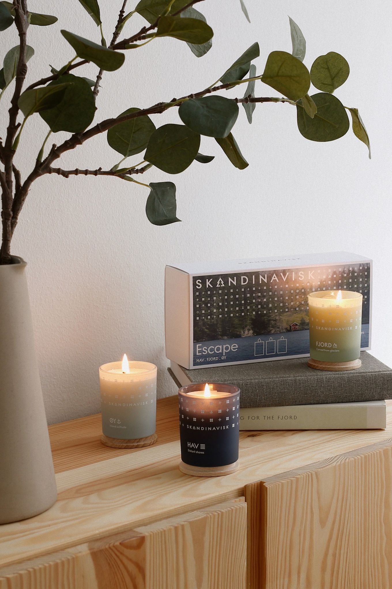 Cadeaux pour la fête des mères : Le coffret Escape trois pièces de Skandinavisk est ici présenté de manière décorative sur une commode en bois.