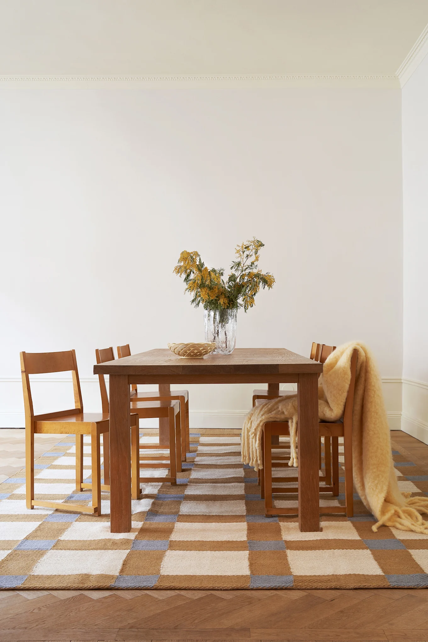 Le jaune beurre est l'une des couleurs tendance pour les intérieurs en 2026. On voit ici un tapis à carreaux Layred dans cette teinte, sur lequel sont disposés une table et des chaises.