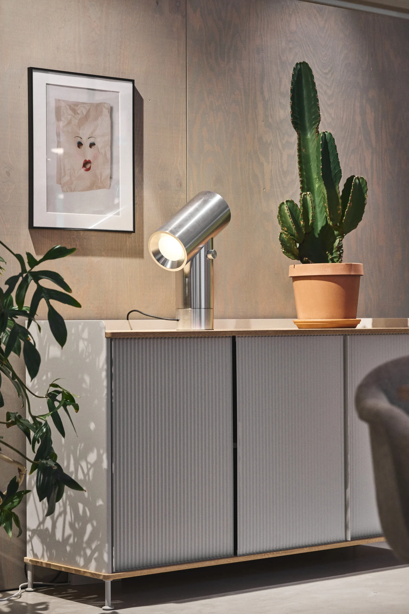 La commode Enfold argentée de Muuto avec un cactus sur le dessus et la lampe de table Beam argentée de Muuto.