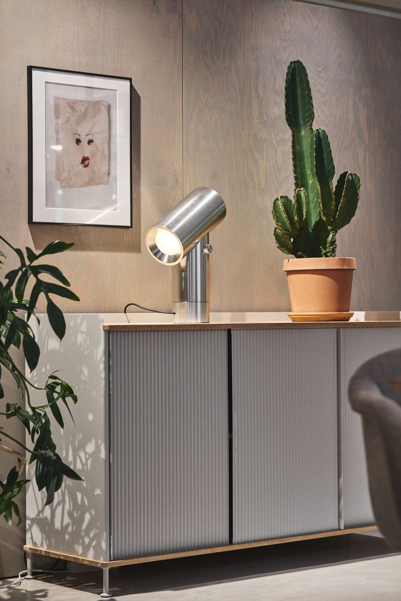La commode Enfold argentée de Muuto avec un cactus sur le dessus et la lampe de table Beam argentée de Muuto.