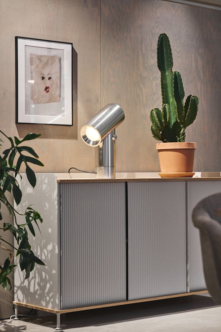 La commode Enfold argentée de Muuto avec un cactus sur le dessus et la lampe de table Beam argentée de Muuto.