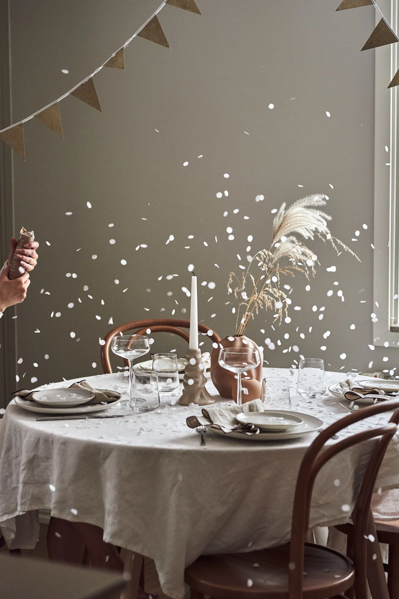 Comment organiser une fête avec l’ambiance parfaite : ici, vous voyez une table dressée, avec un pétard de fête qui vient d’exploser et des confettis qui retombent doucement sur la table.