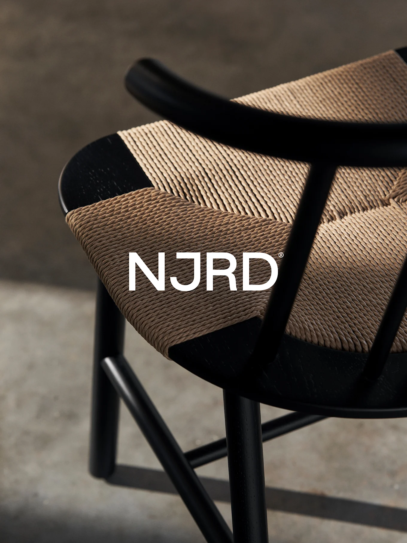 Gros plan d'une chaise noire avec une assise tressée marron clair, ornée du logo blanc 'NJRD'.