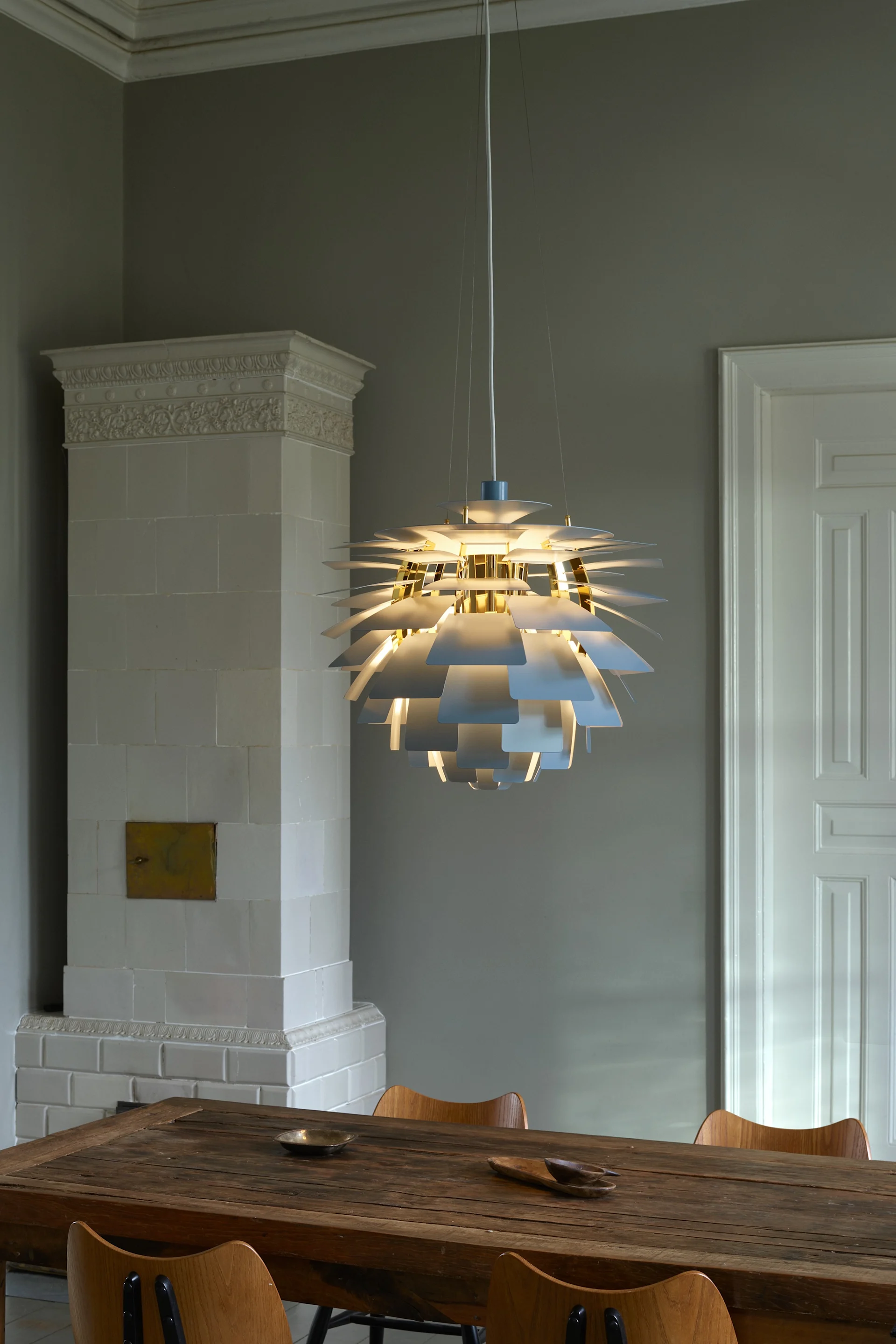 Une lampe suspendue radiante à plusieurs couches avec des accents blancs et dorés, éclairant une table à manger rustique en bois.