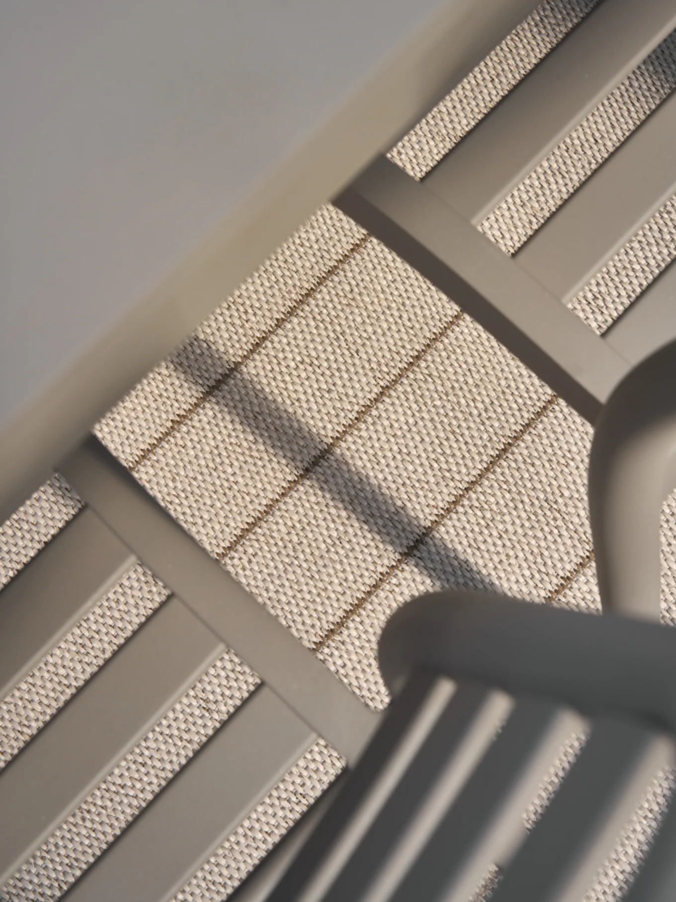 Gros plan, vue en angle d'un matériau tissé beige clair avec de subtiles rayures brunes horizontales et diagonales, encadré par des barres grises lisses.