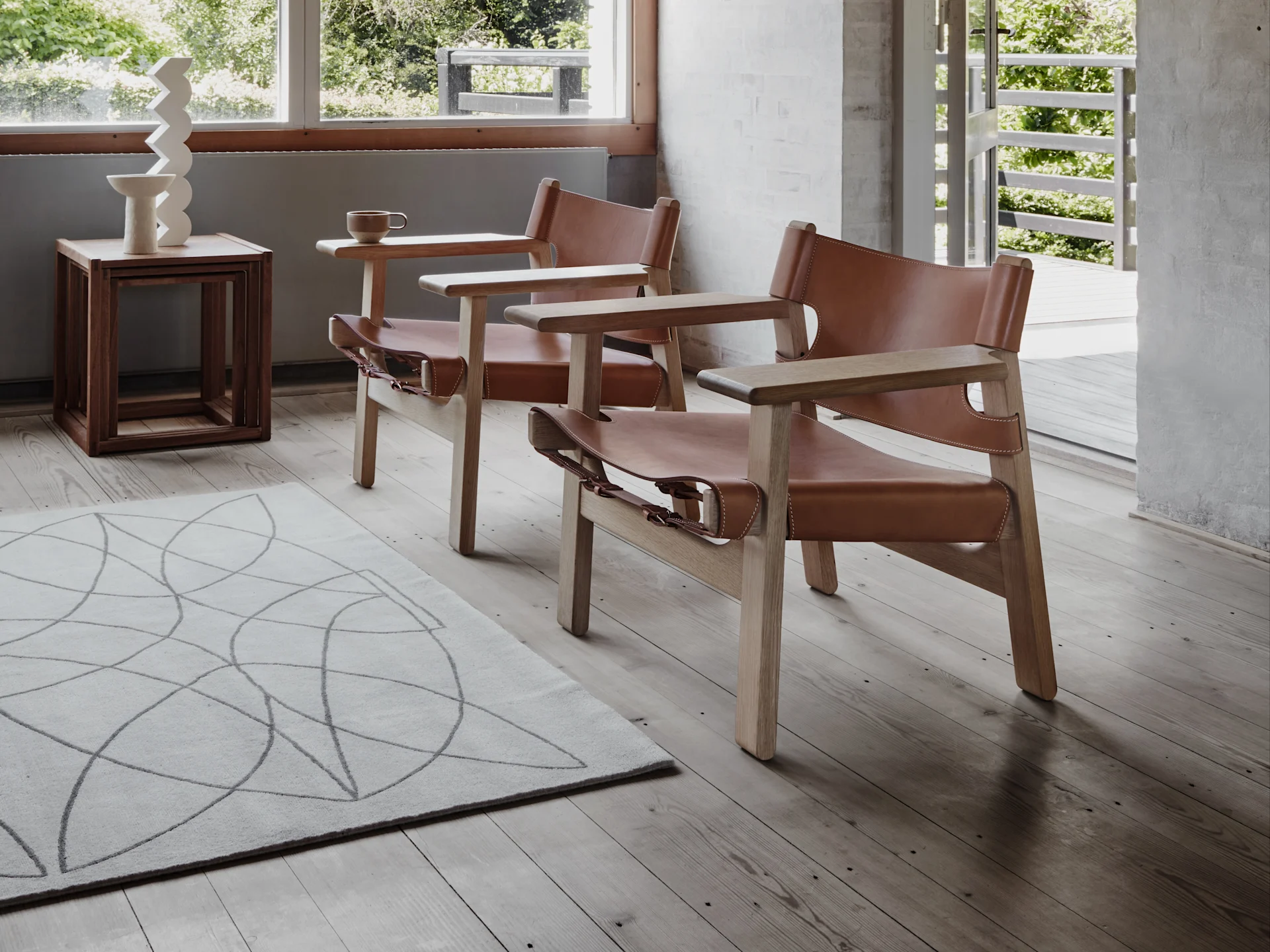 Un fauteuil moderne en bois clair et cuir marron à côté d'une table ronde en bois sur un sol en béton avec de la lumière du soleil.