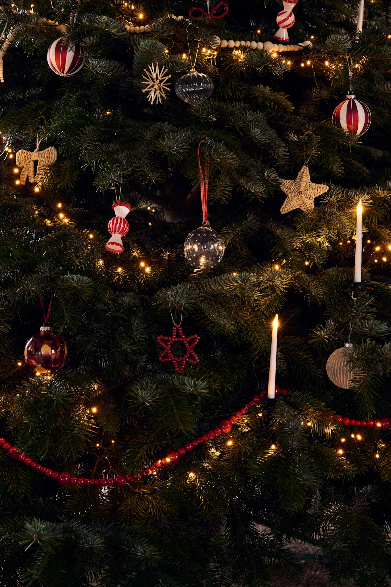 Un sapin de Noël richement décoré avec diverses ornements, des guirlandes lumineuses chaudes et des bougies allumées.