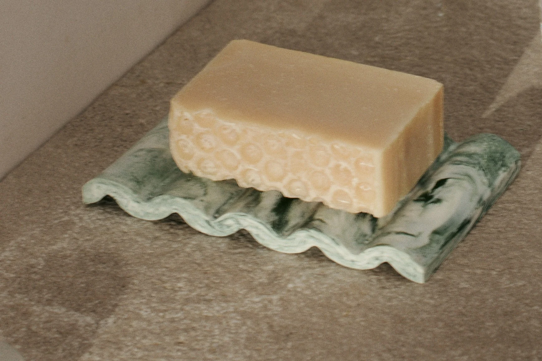 Pain de savon beige clair texturé en nid d'abeille sur un porte-savon ondulé marbré vert.