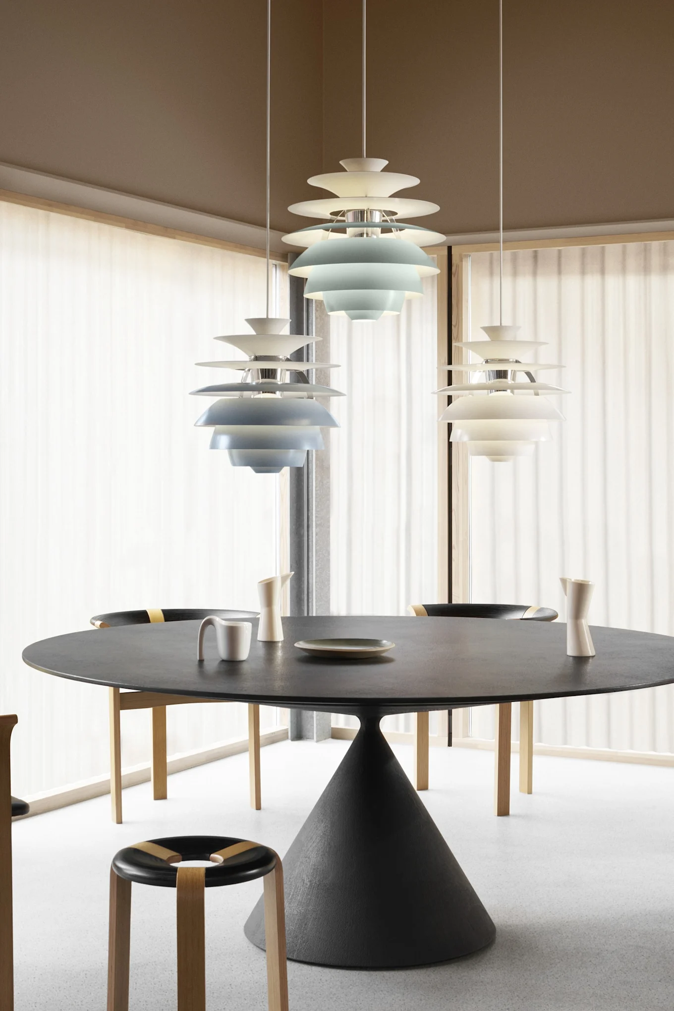 Salle à manger moderne avec table ronde noire, chaises et trois suspensions étagées, deux bleues et une blanche.