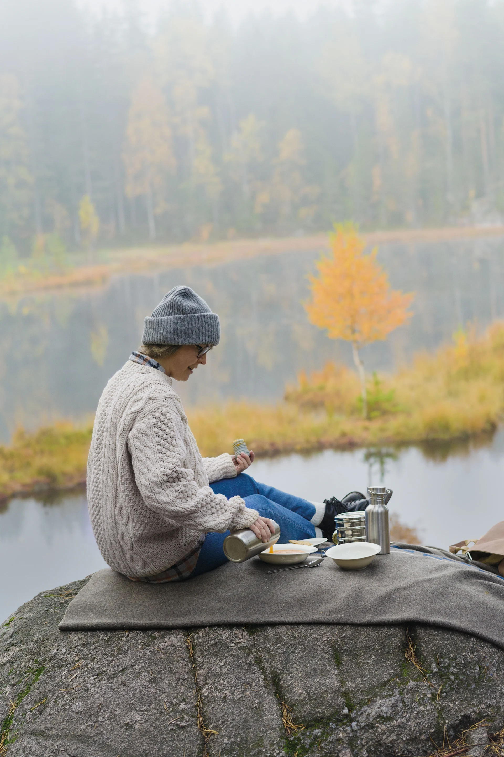 Lagom : une femme fait un pique-nique sur une montagne, tout autour on peut voir un paysage automnal.