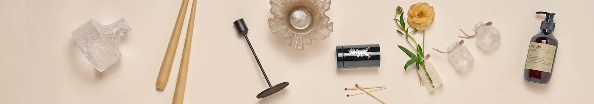 Une collection d'articles de décoration intérieure, comprenant des vases en verre, des baguettes, un chandelier noir, un bol en verre plissé, un récipient noir, une fleur orange et une bouteille de lotion pour les mains.