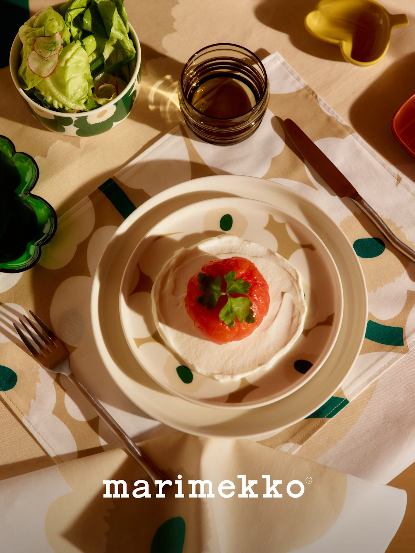 Table Marimekko avec saladier à motifs, plat de fruits rouges et crème, verre et couverts sur une nappe fleurie.