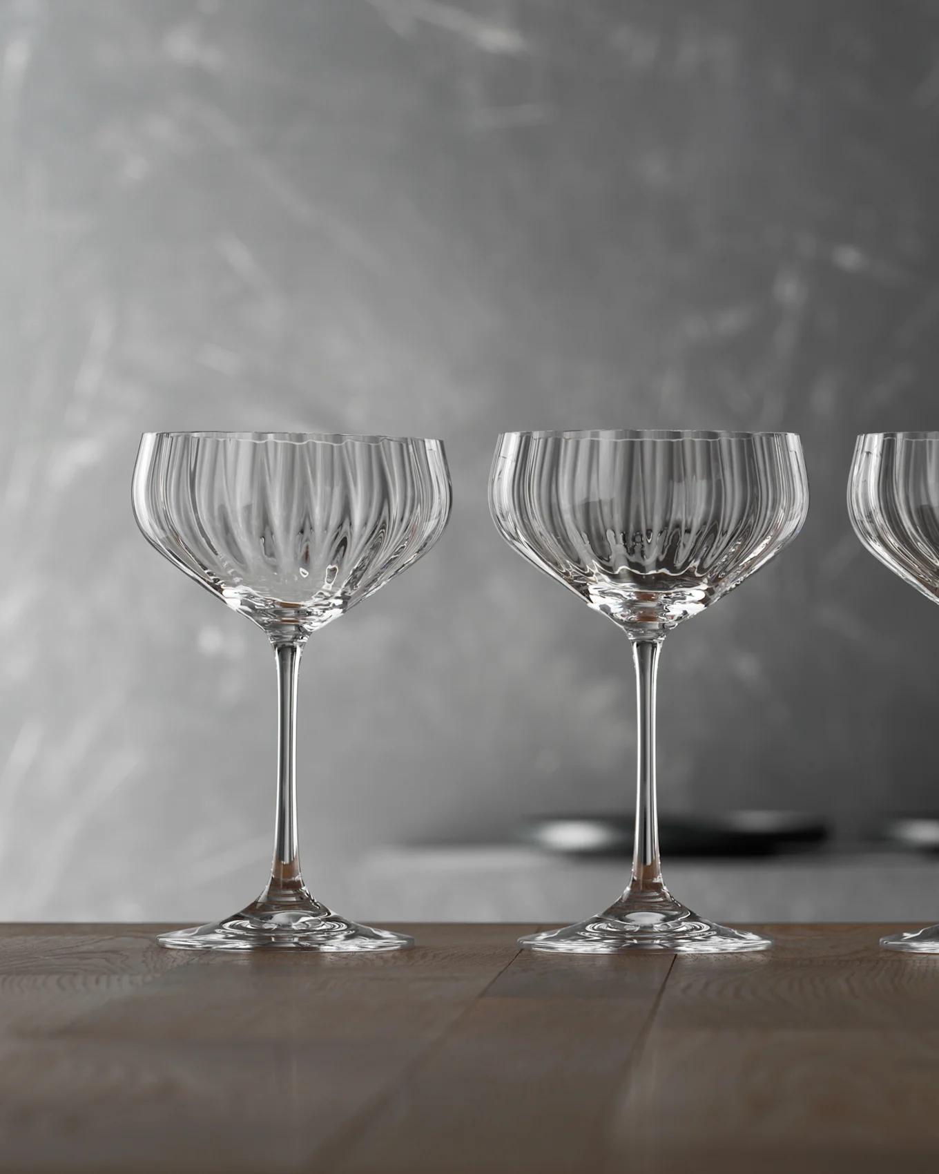 Trois coupes de champagne vides, claires et nervurées sur une table en bois avec un fond gris.