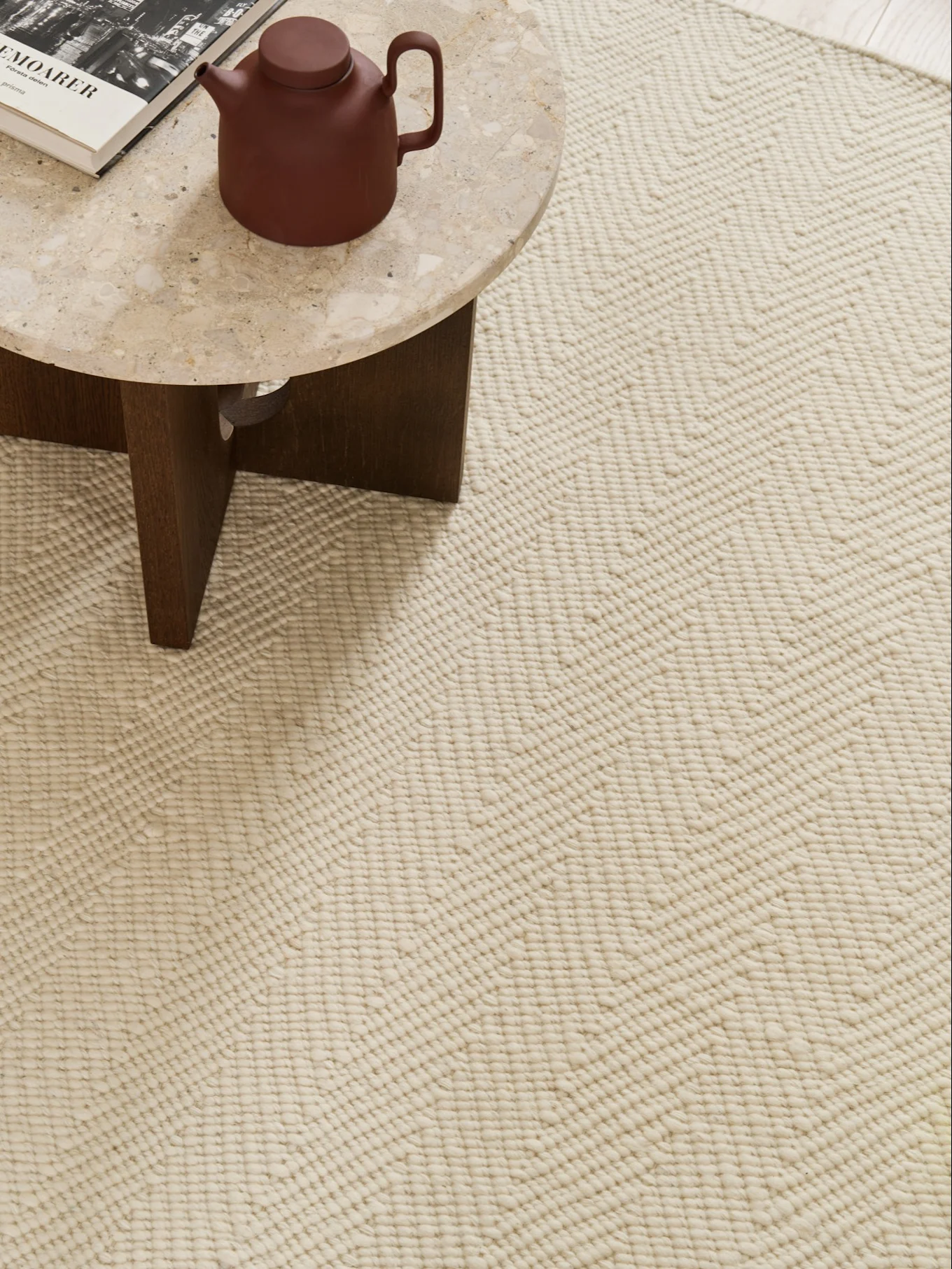 Gros plan d'un tapis crème au motif zigzag texturé, avec une table en marbre, une théière et un livre dans le coin.