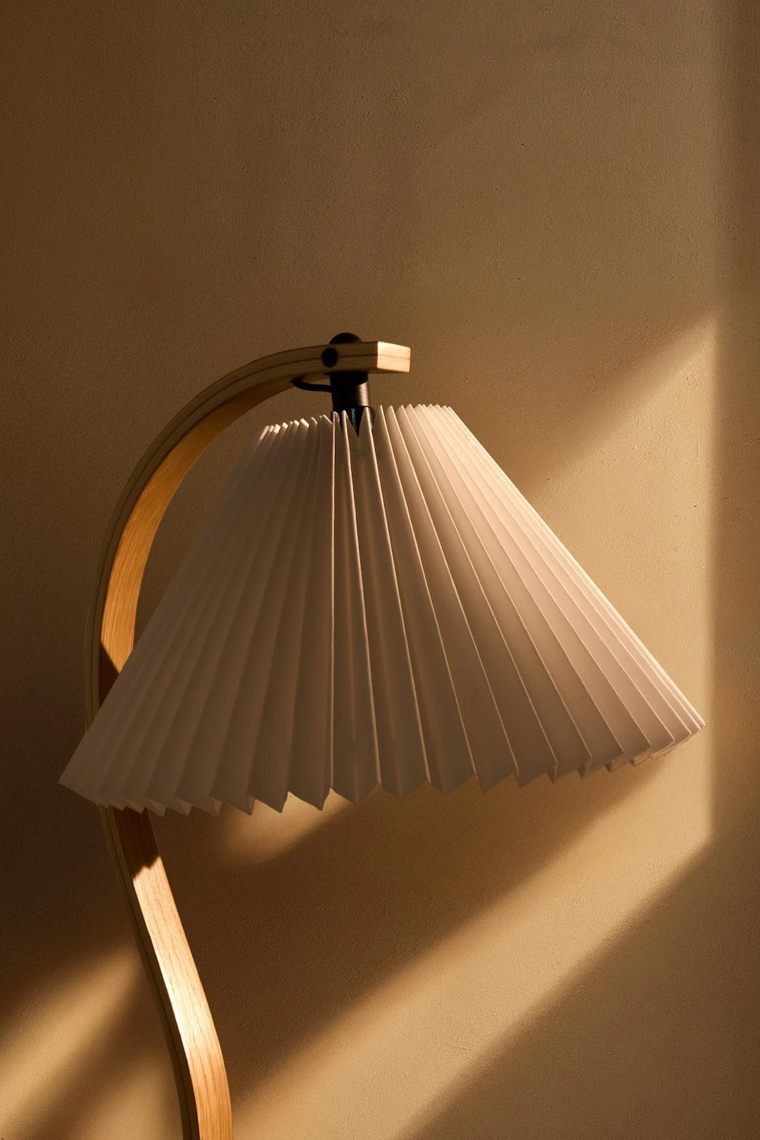 Une lampe dotée d'un abat-jour plissé blanc et d'un pied en bois incurvé, qui diffuse une lumière chaleureuse sur un mur texturé.