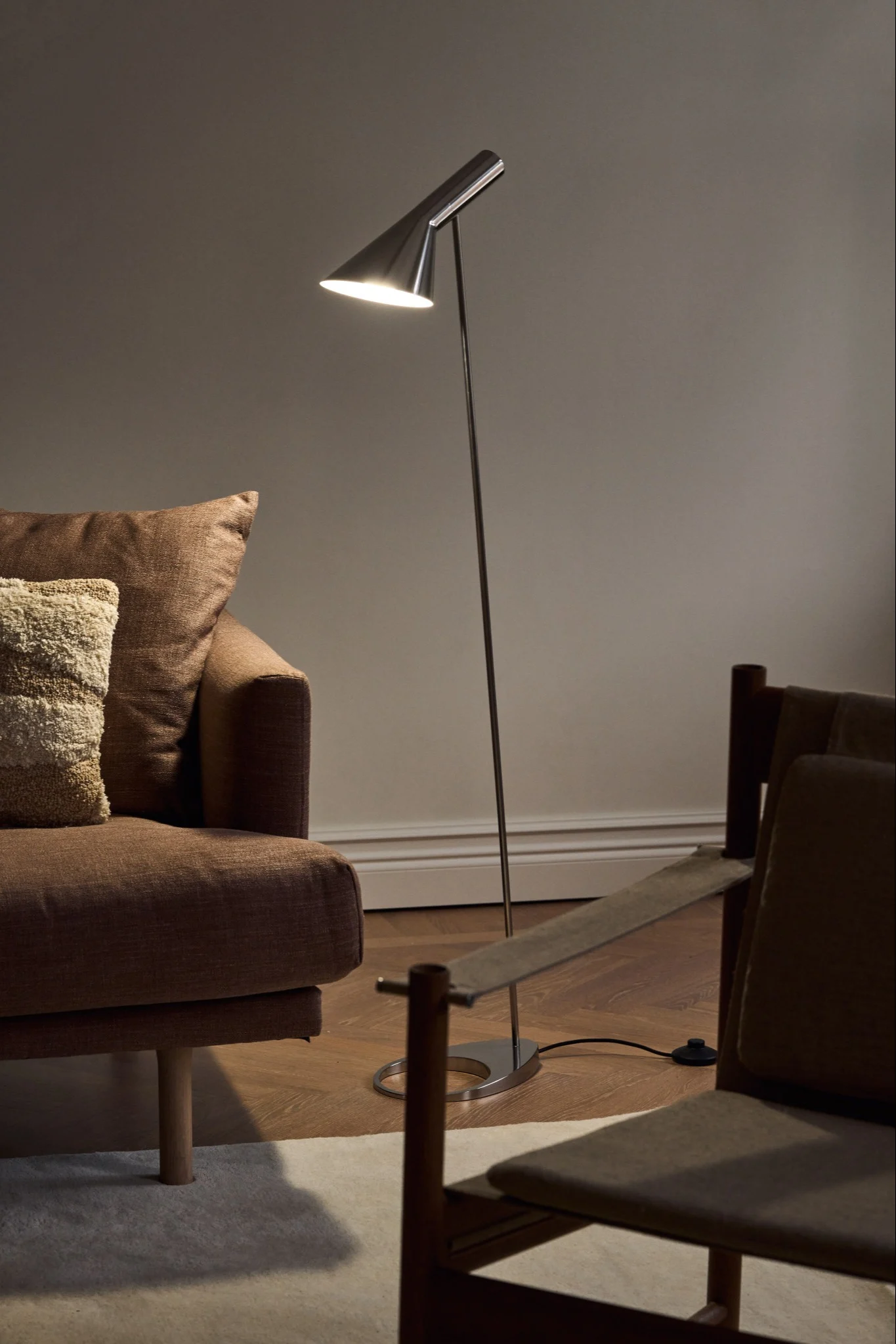 Lampes scandinaves : le lampadaire AJ chromé de Louis Poulsen trône dans un salon sobre, à côté d'un canapé.