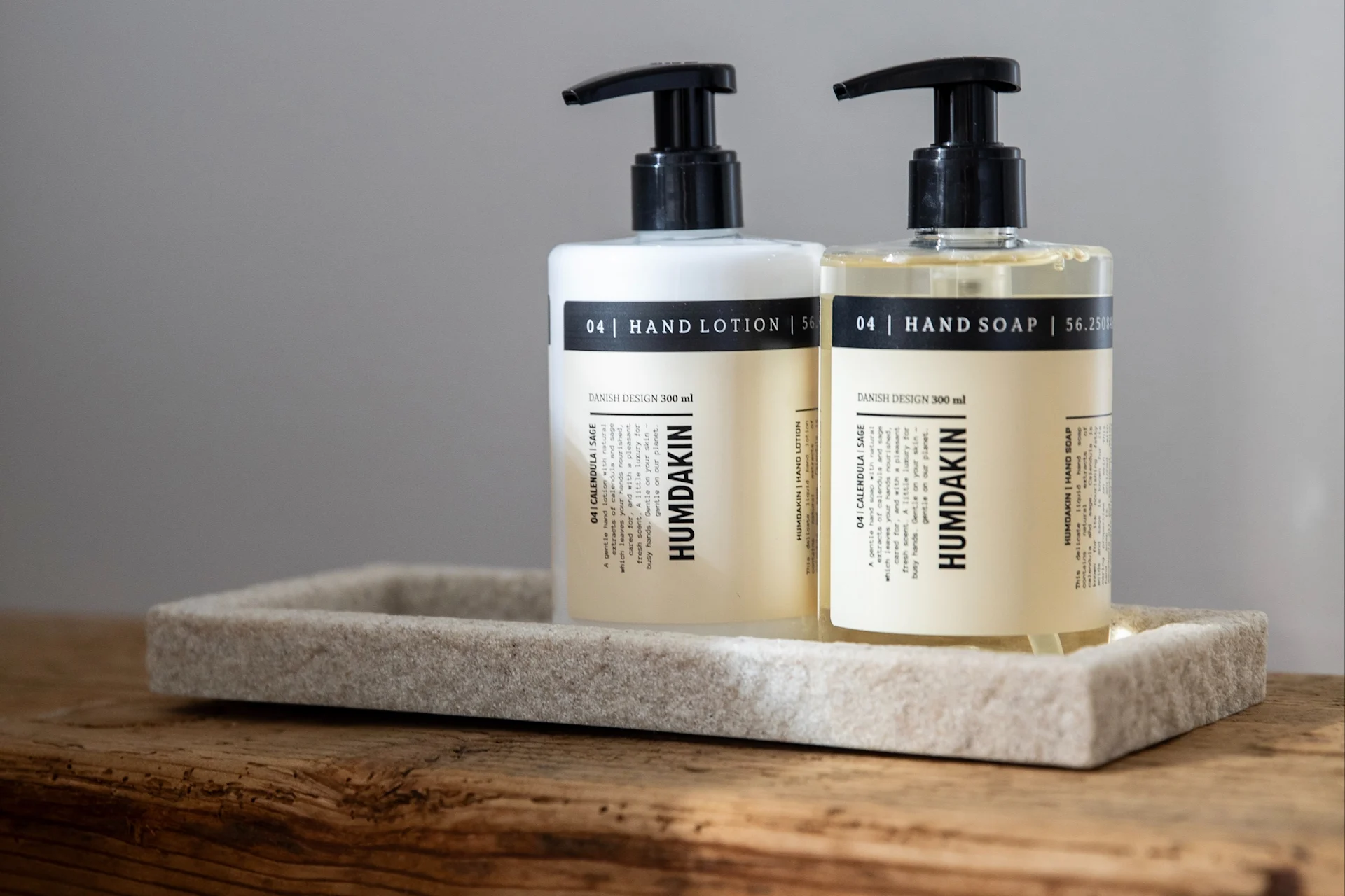 Deux flacons pompe Humdakin, lotion pour les mains (blanc) et savon pour les mains (transparent), sur un plateau en pierre sur bois.