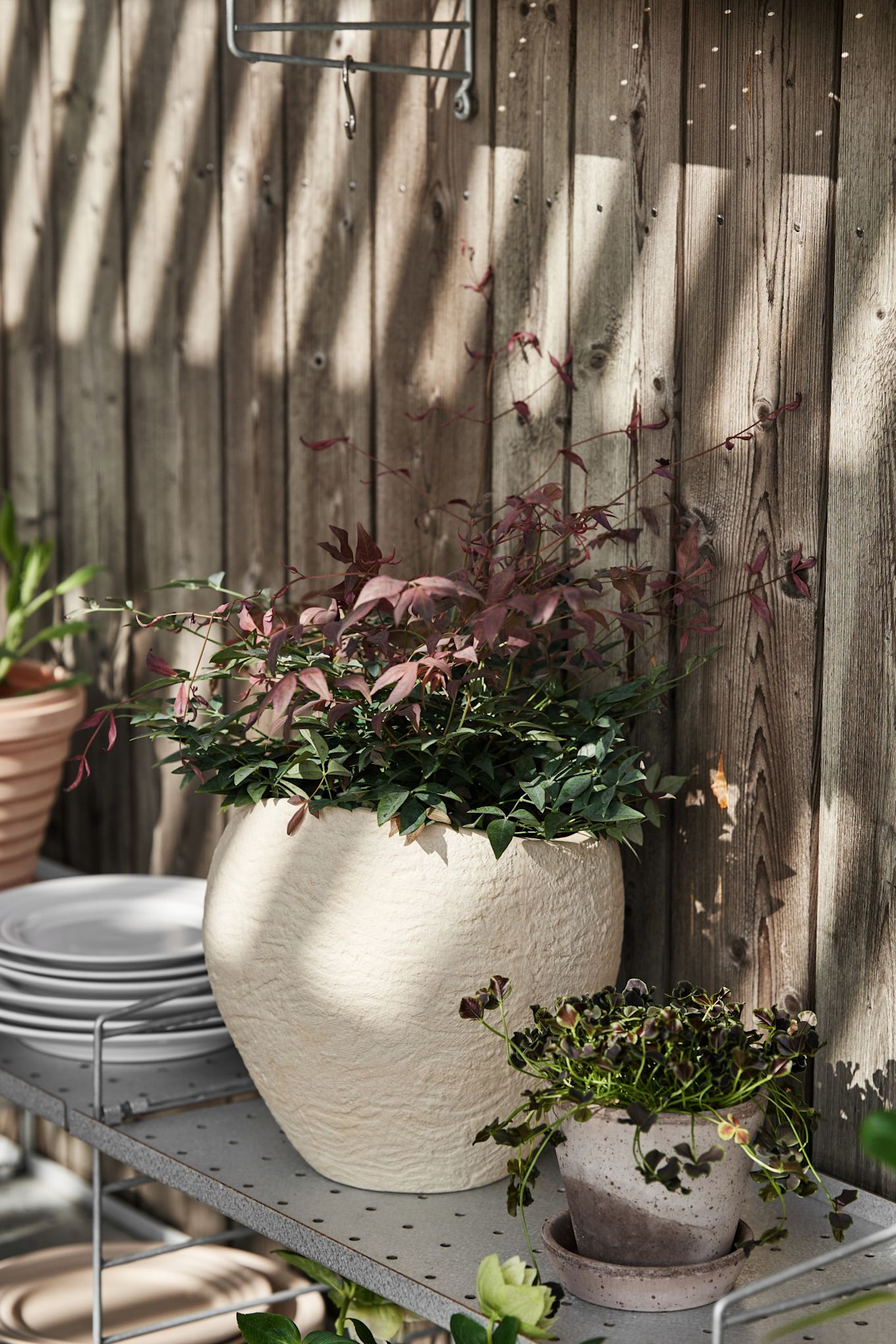 Une étagère String sur une terrasse, sur laquelle se trouve le grand pot de fleurs Plantas d'Audo Copenhagen.