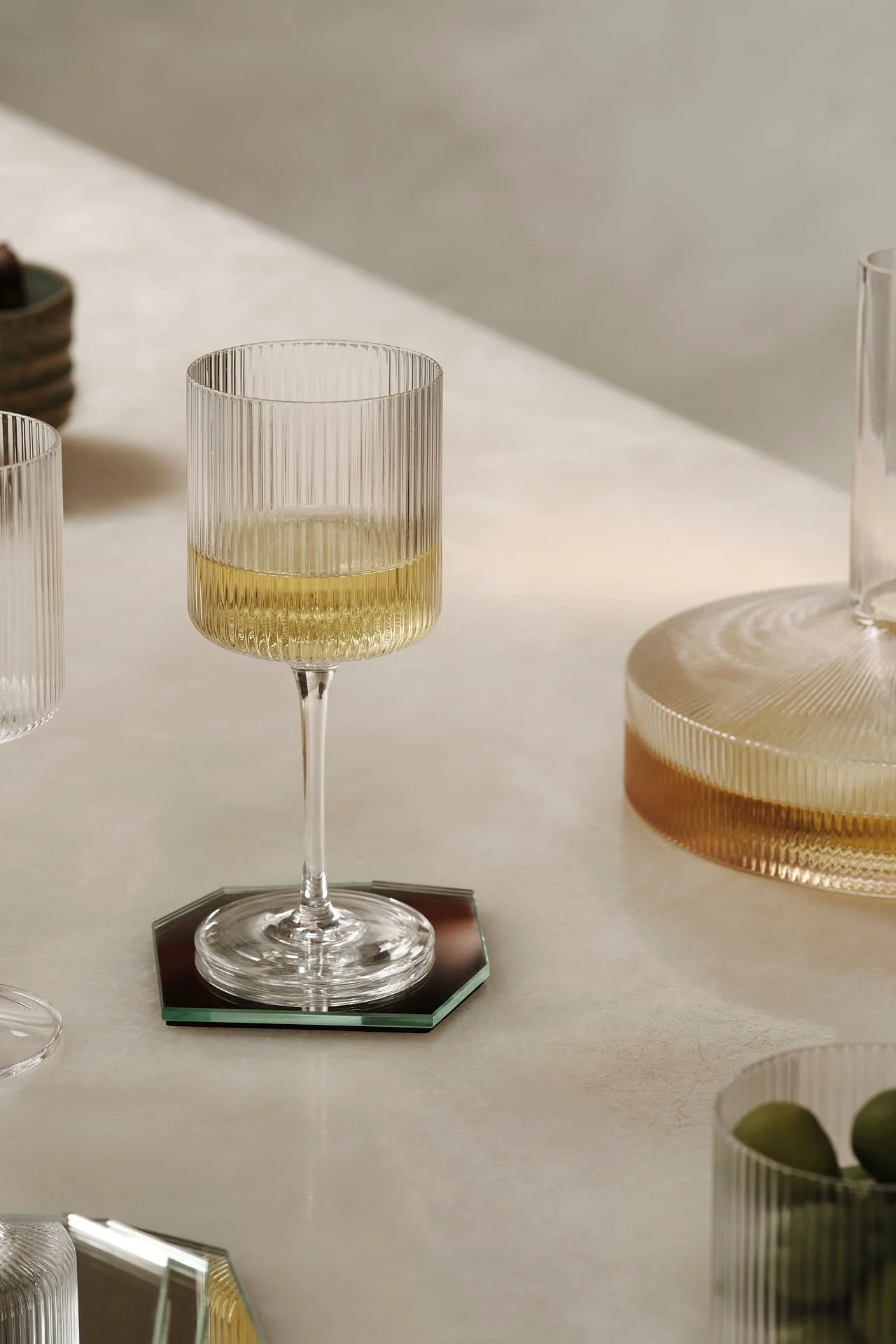 Un verre à vin cannelé avec du vin blanc sur un dessous de verre hexagonal miroir.