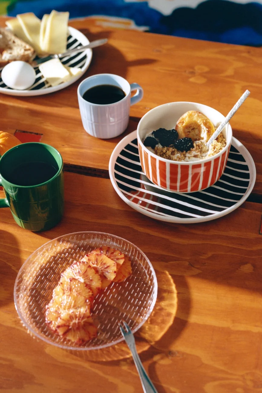 Petit-déjeuner sur table en bois avec vaisselle rayée, café, flocons d'avoine, fromage, pain, œuf et oranges sanguines.