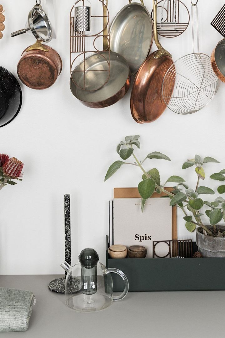 La théière Still de Ferm Living est simple mais stylée. Elle est ici posée sur un comptoir de cuisine, des casseroles sont suspendues au-dessus.