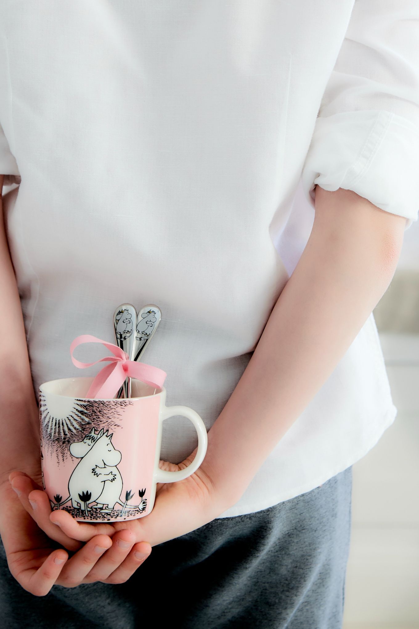 Un garçon cache la tasse Moomin 'Love' de Moomin Arabia avec les cuillères Moomin 'Love' de Hackman derrière son dos.