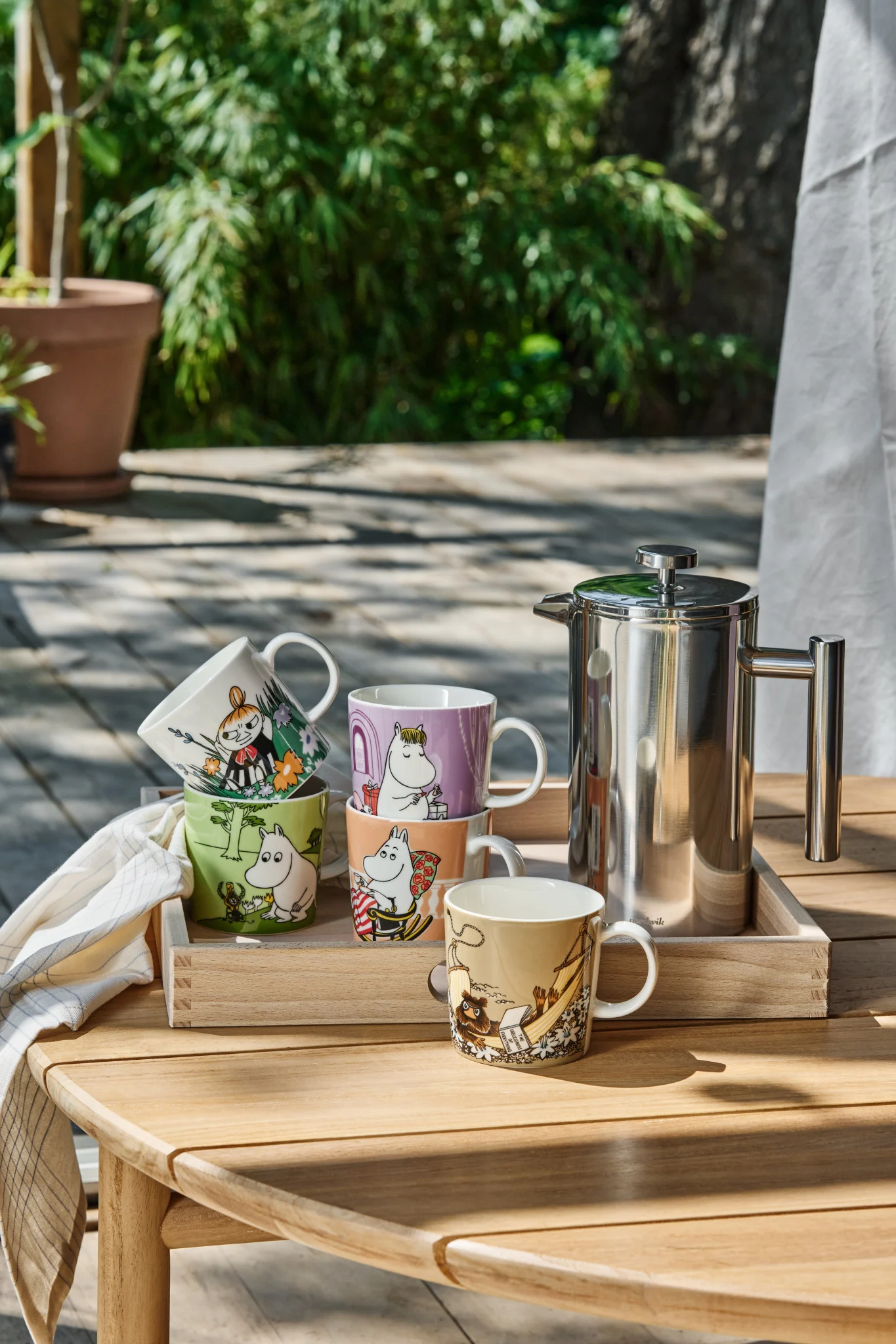 Plusieurs tasses de Moomin sont posées sur une table dans le jardin.