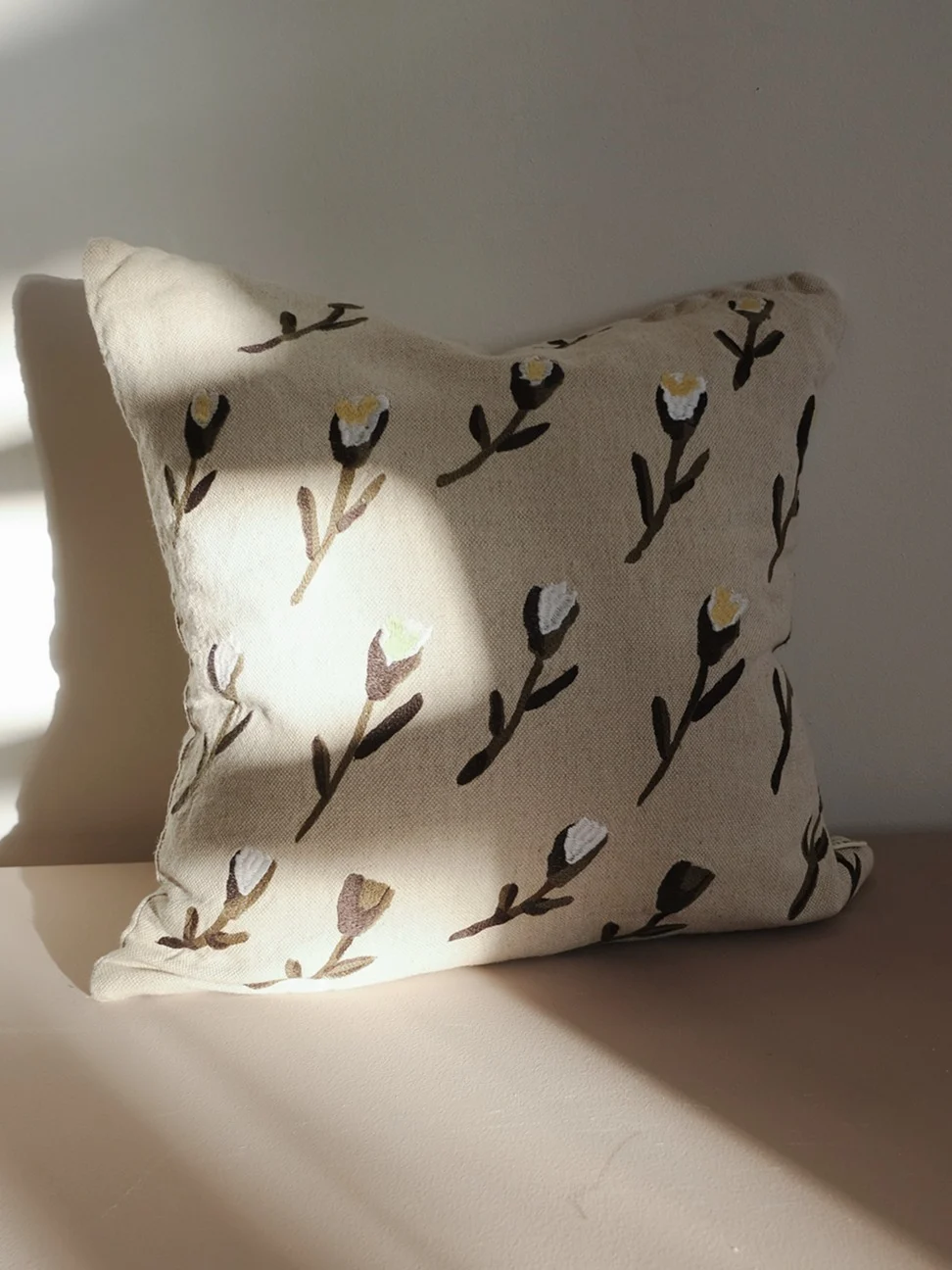Coussin beige clair avec un motif de fleurs stylisées marron foncé et blanches.