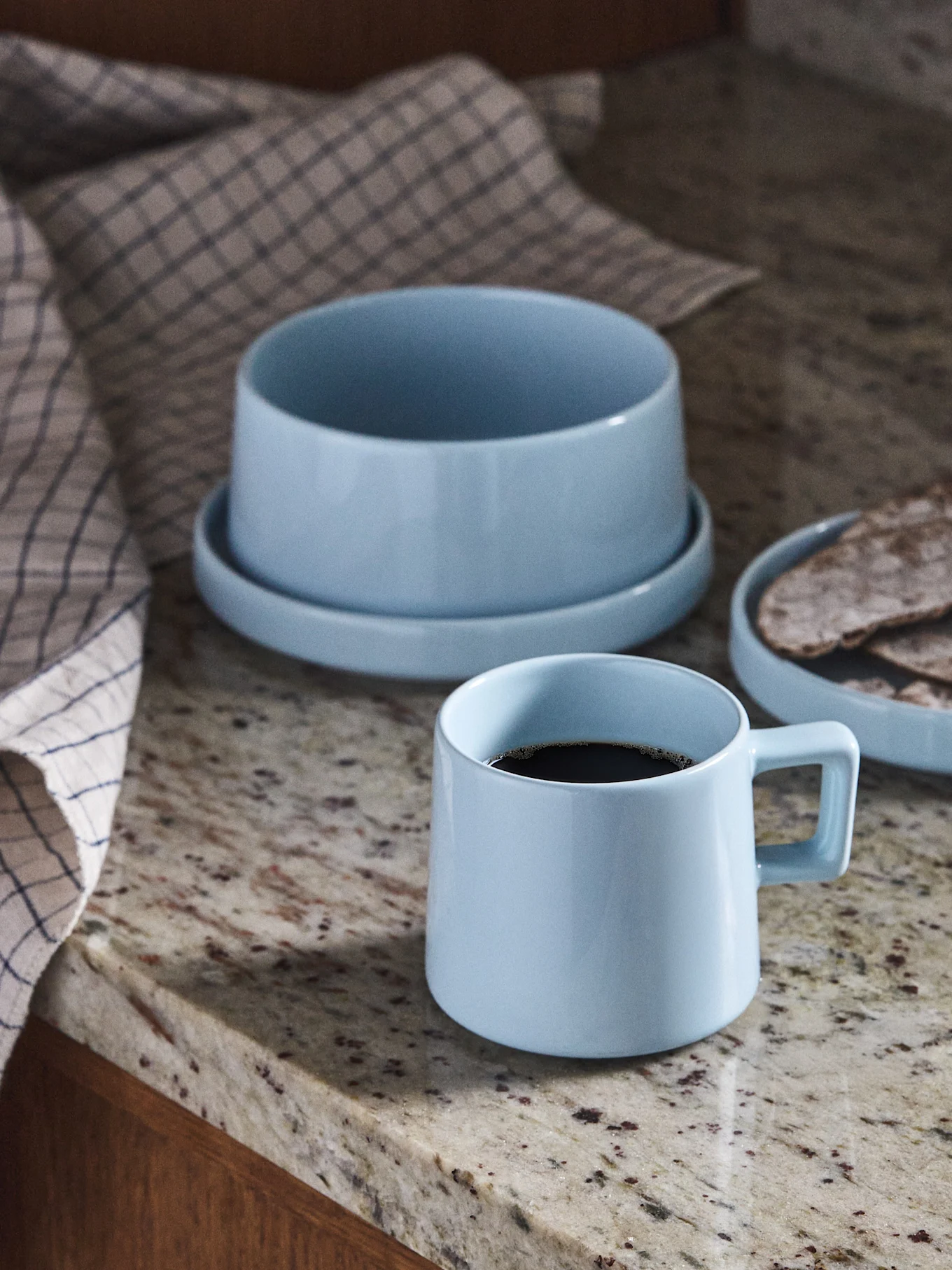 Mug à café en céramique bleu clair, bol et assiette avec pain plat sur un comptoir en granit.