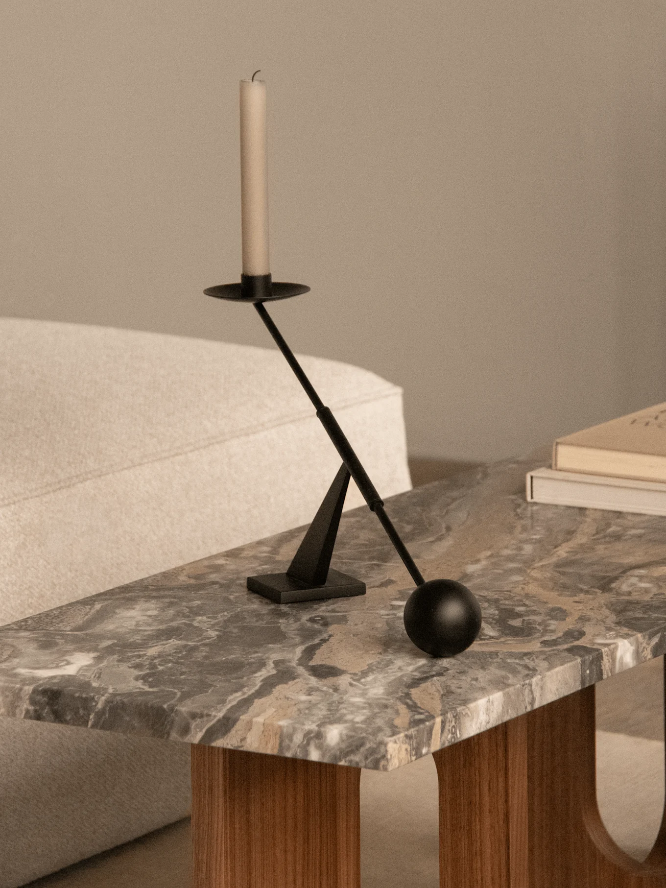Un bougeoir moderne noir avec une bougie blanche sur une table basse en marbre à côté de deux livres et un canapé clair.