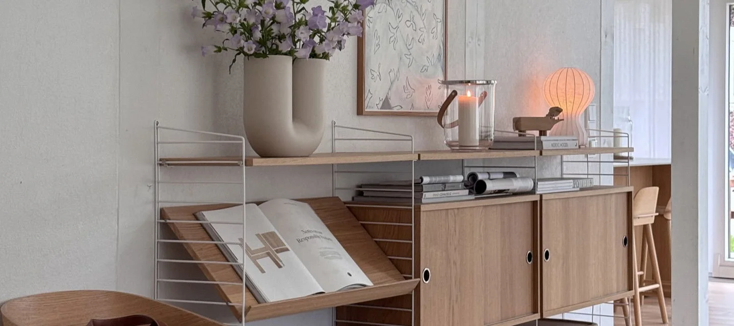 Étagère modulaire avec cadres blancs, étagères, armoires, vase à fleurs, bougie dans lanterne et lampe champignon.
