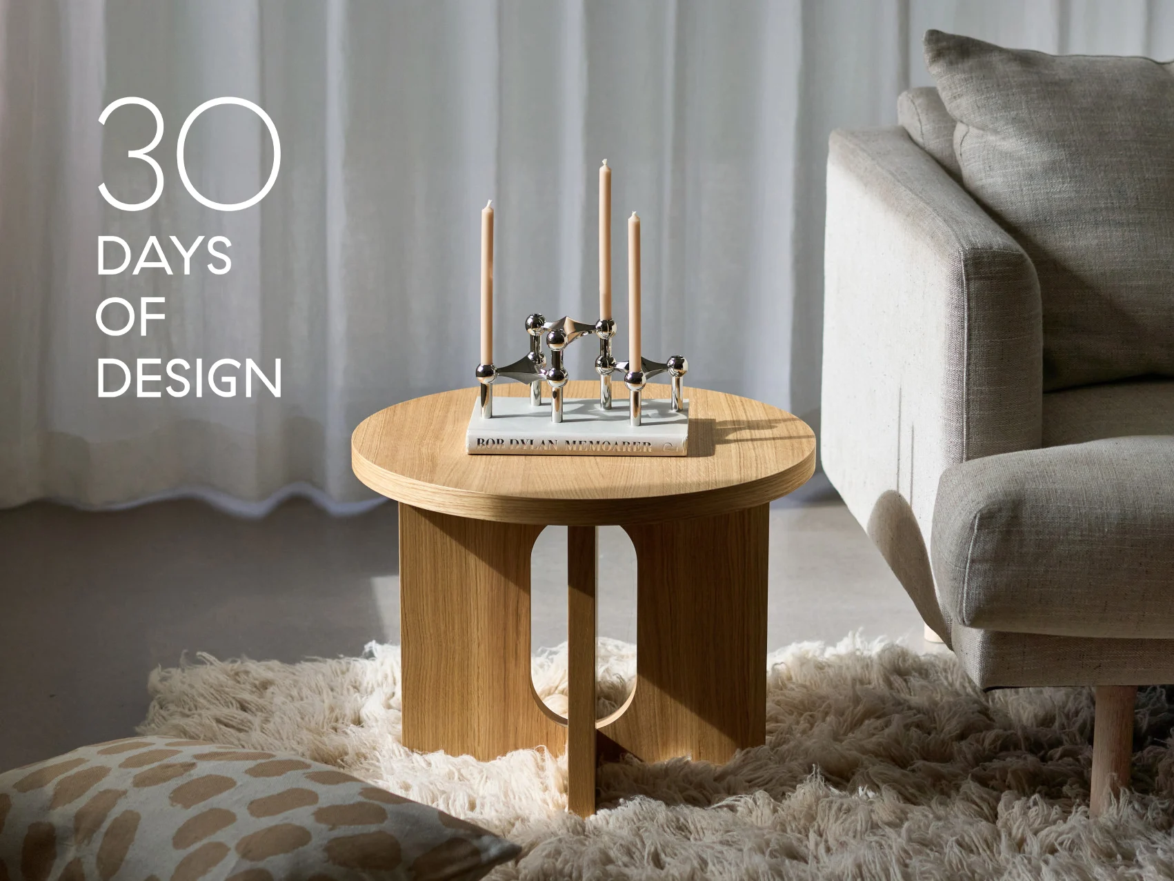 Salon moderne avec table d'appoint ronde en bois, chandelier argenté à trois bougies, un livre et un canapé beige. Texte: '30 JOURS DE DESIGN'.