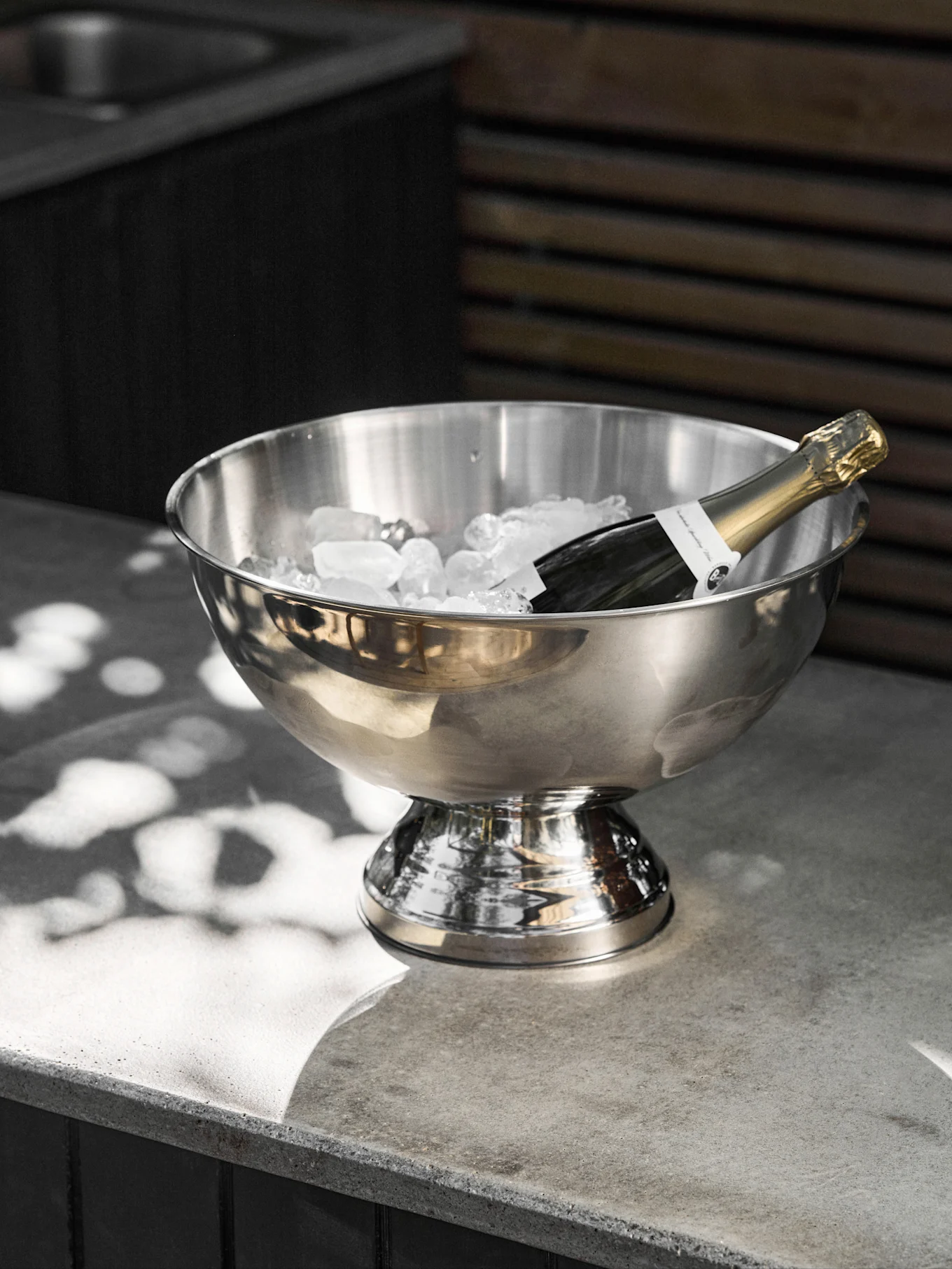 Bouteille de champagne refroidie dans un seau à glace en acier inoxydable sur une surface en béton.