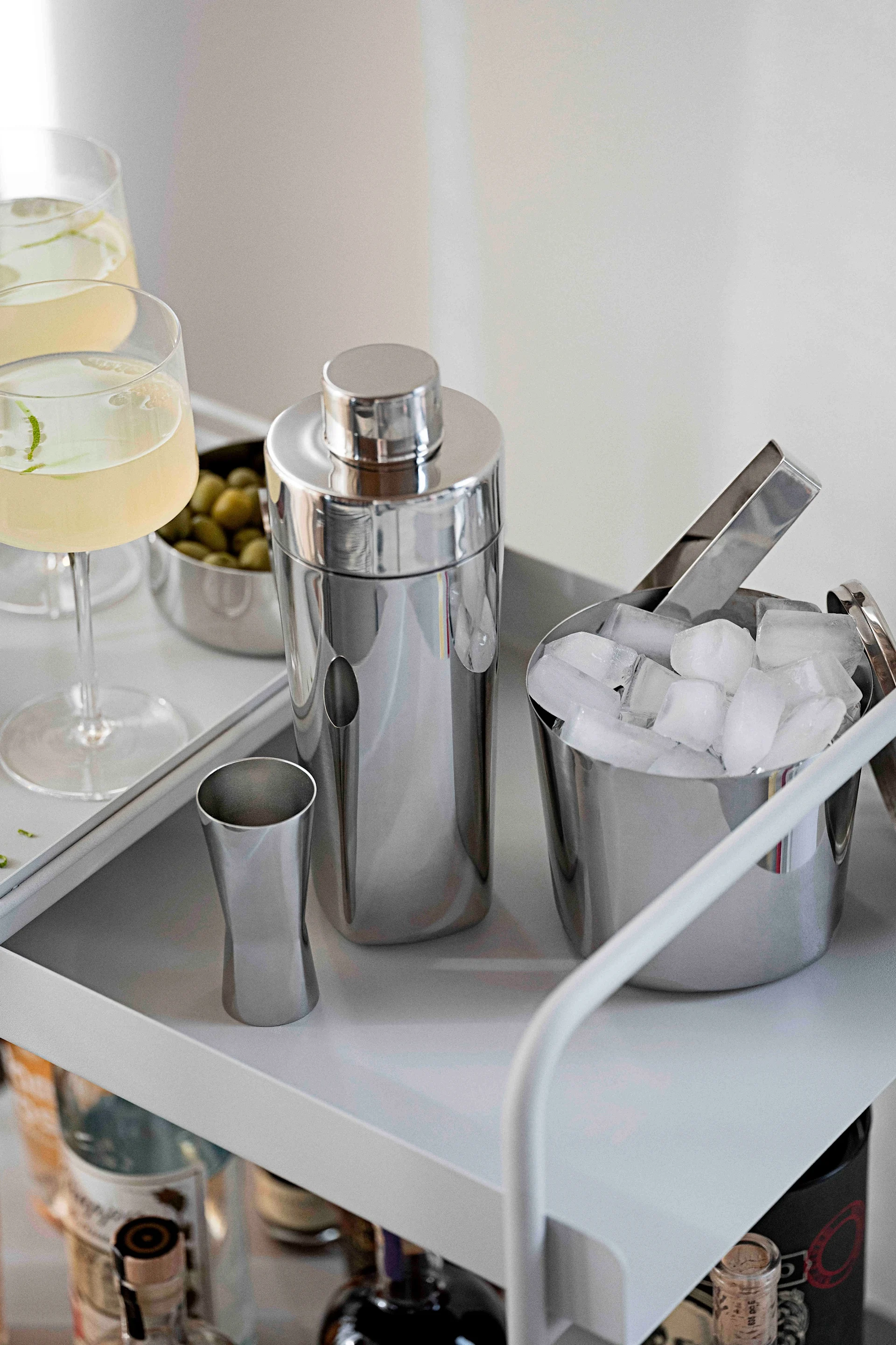 Les accessoires professionnels pour cocktails sont également recommandés pour les cocktails sans alcool. Ici, le shaker, le verre doseur et le seau à glace de la collection Rocks de Zone Denmark sont posés sur un chariot de bar.