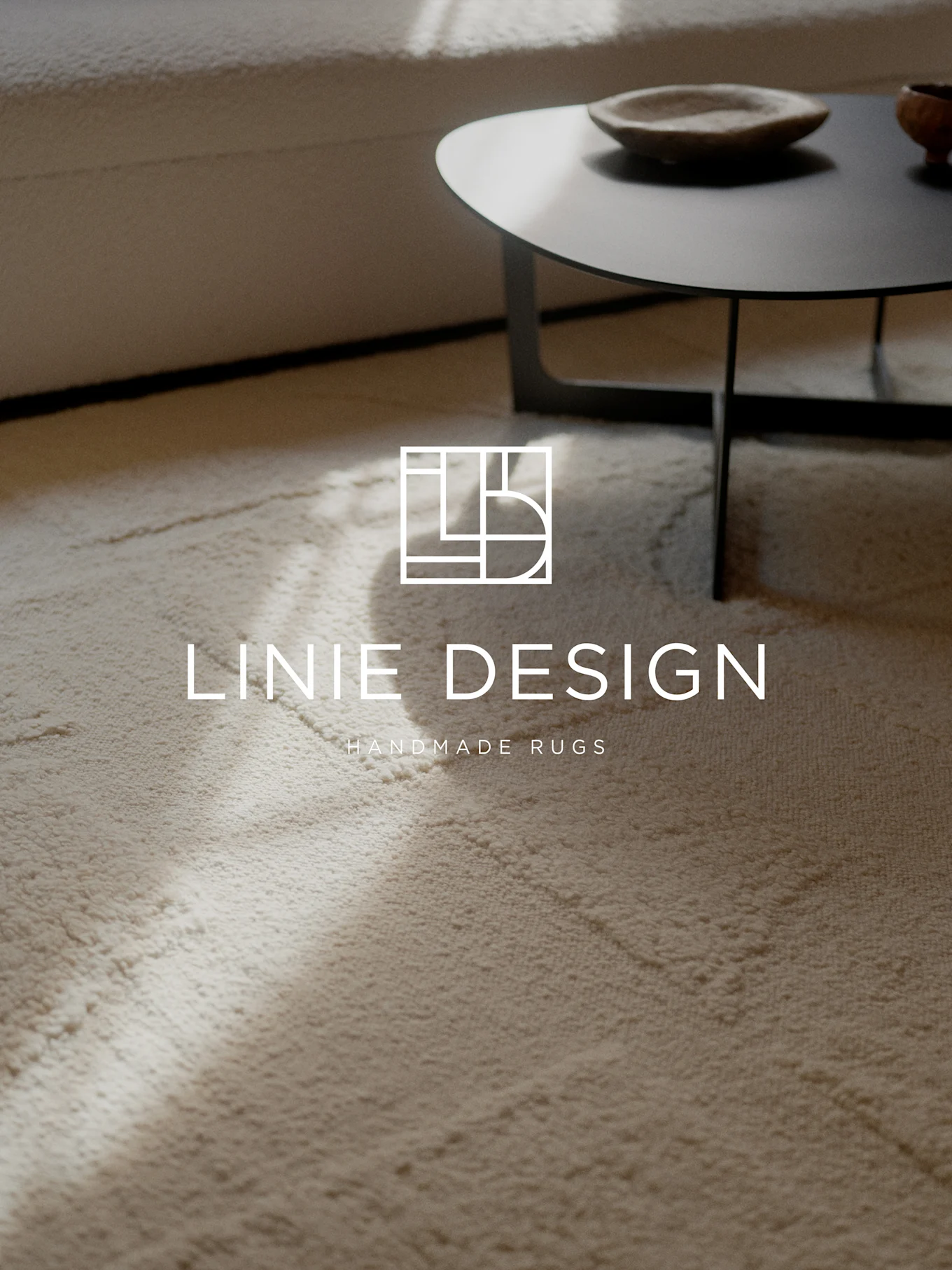 Un tapis clair texturé avec le logo et le texte 'Linie Design Handmade Rugs'. Un canapé et une table basse flous en arrière-plan.
