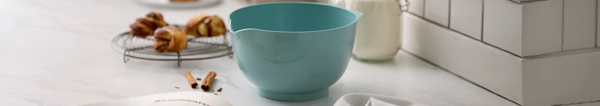 Bol mélangeur bleu clair, pâtisseries sur grille, bouteille de lait et livre de recettes sur comptoir en marbre.