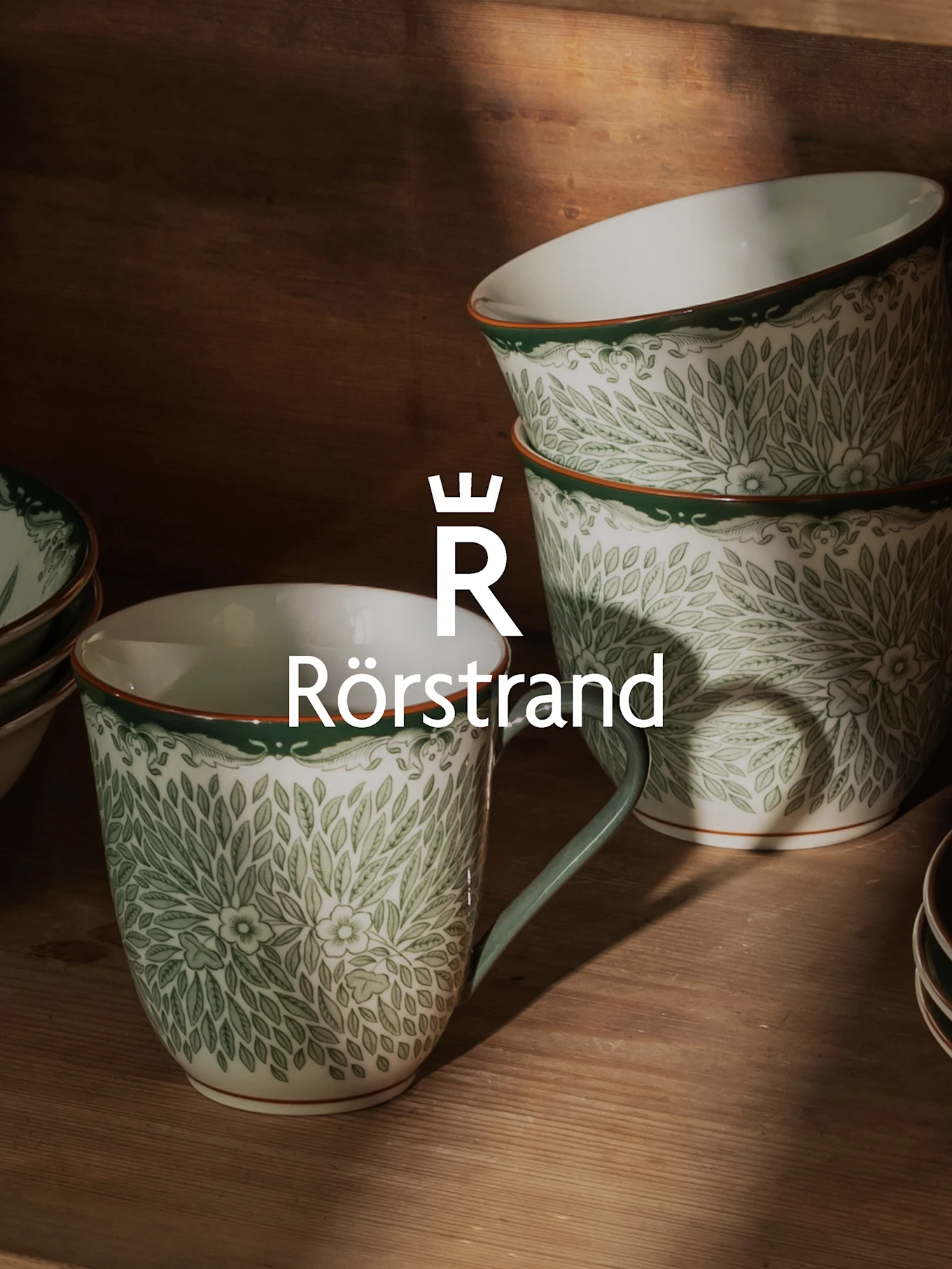 Tasses et bols en céramique blancs à motif de feuilles vertes, bord orange et logo Rörstrand.