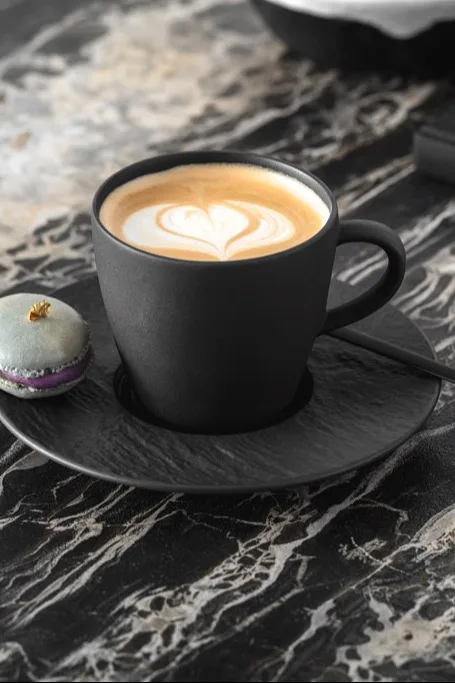 Une tasse de café noir avec un dessin de lait mousseux sur le dessus.