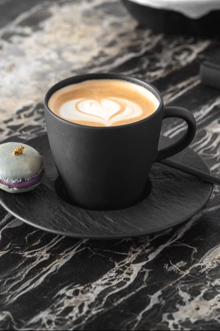Une tasse de café noir avec un dessin de lait mousseux sur le dessus.