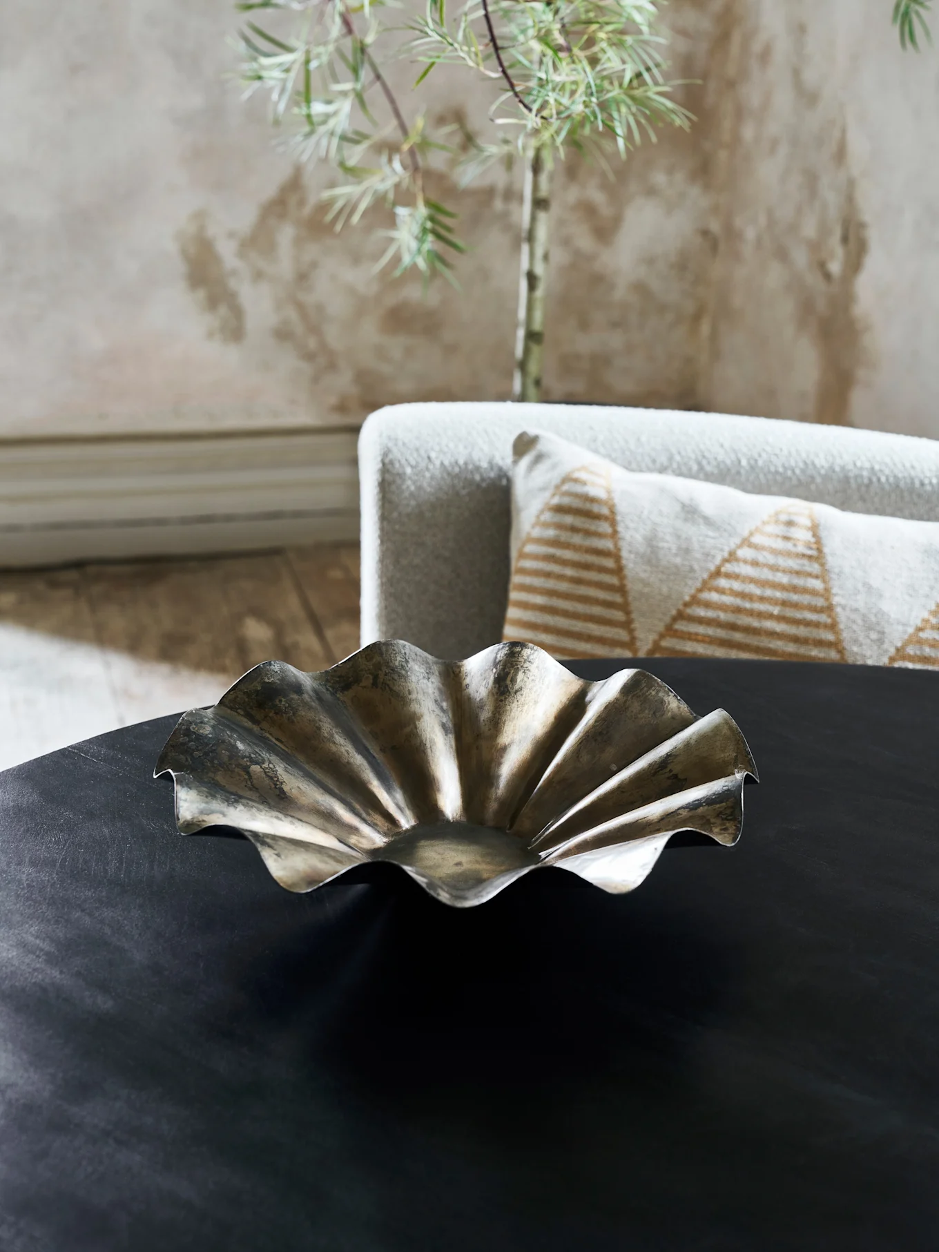 Un bol décoratif métallique avec un bord ondulé et volanté sur une table sombre dans un salon.