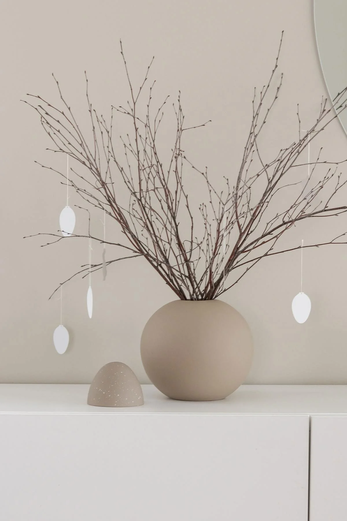 Un arbuste de Pâques se trouve également sur une commode blanche dans un vase Ball de couleur sable avec des pendentifs d'œufs Easter Deco, tous deux de Cooee Design, dans la maison de @tunadalen.