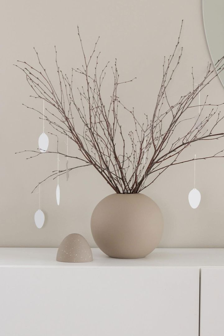 Un arbuste de Pâques se trouve également sur une commode blanche dans un vase Ball de couleur sable avec des pendentifs d'œufs Easter Deco, tous deux de Cooee Design, dans la maison de @tunadalen.