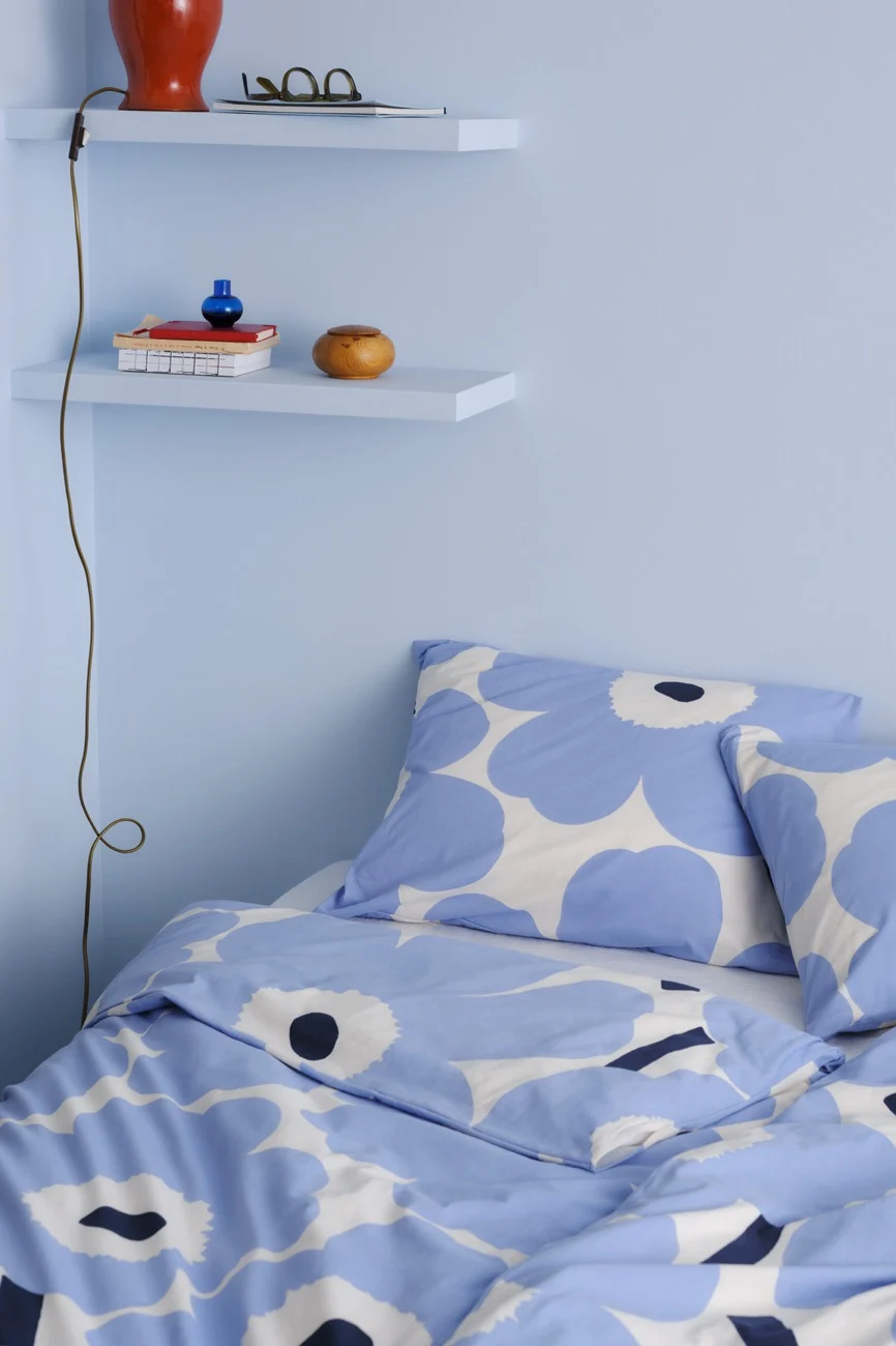 Un coin chambre avec des murs bleu clair, deux étagères flottantes et un lit avec une parure de lit florale bleue et blanche.