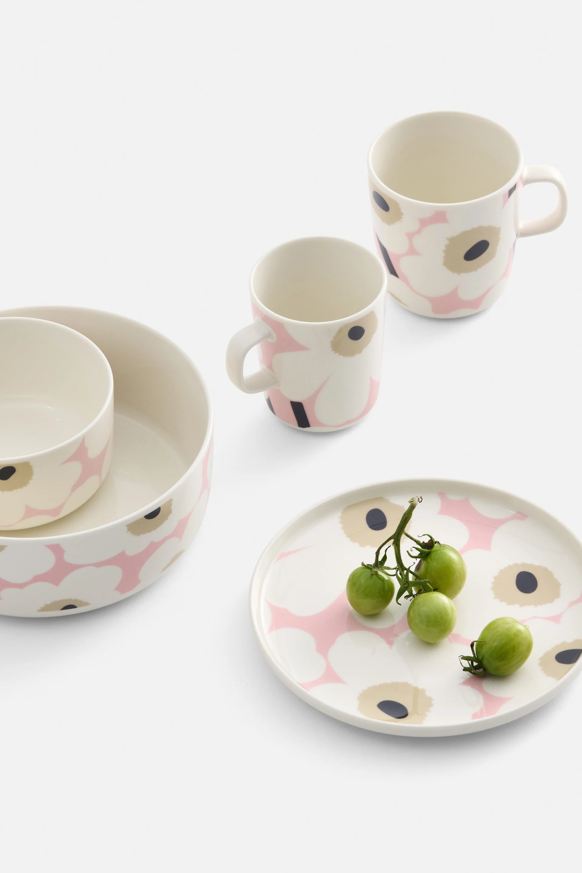 Vaisselle couleur crème avec motif floral rose et noir, comprenant deux bols, deux tasses et une assiette avec des tomates cerises vertes.