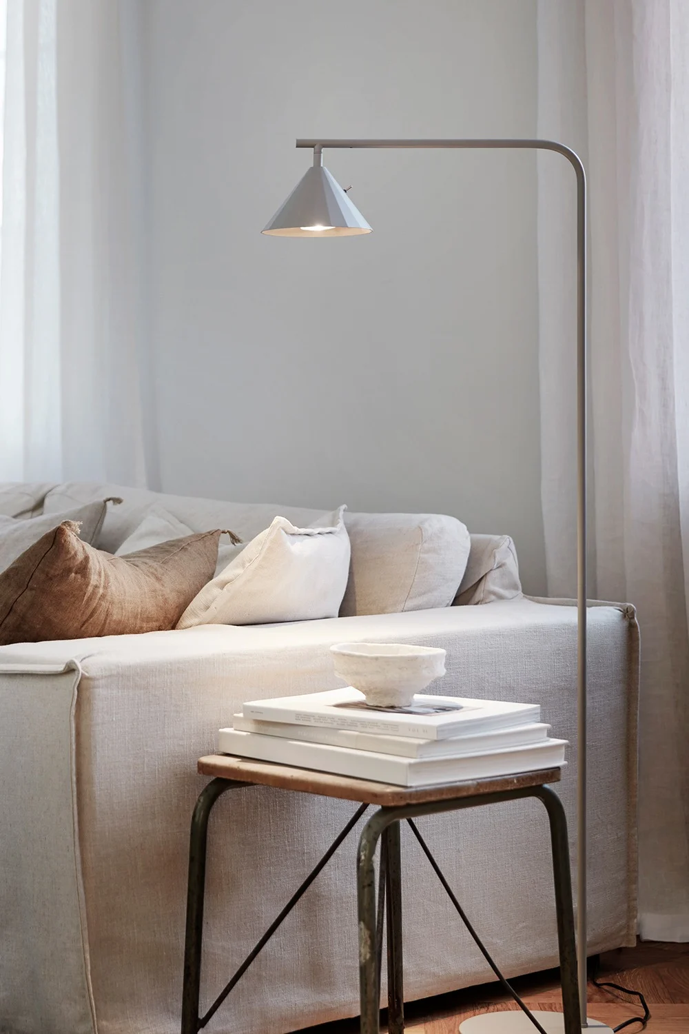 Un salon confortable avec un canapé en lin clair, un lampadaire et une table d'appoint avec des livres et un bol.