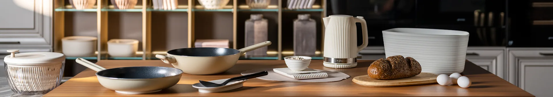 Comptoir de cuisine avec poêles beige, une bouilloire électrique blanche côtelée, un pain aux graines sur une planche et des œufs. Accessoires de cuisine modernes.